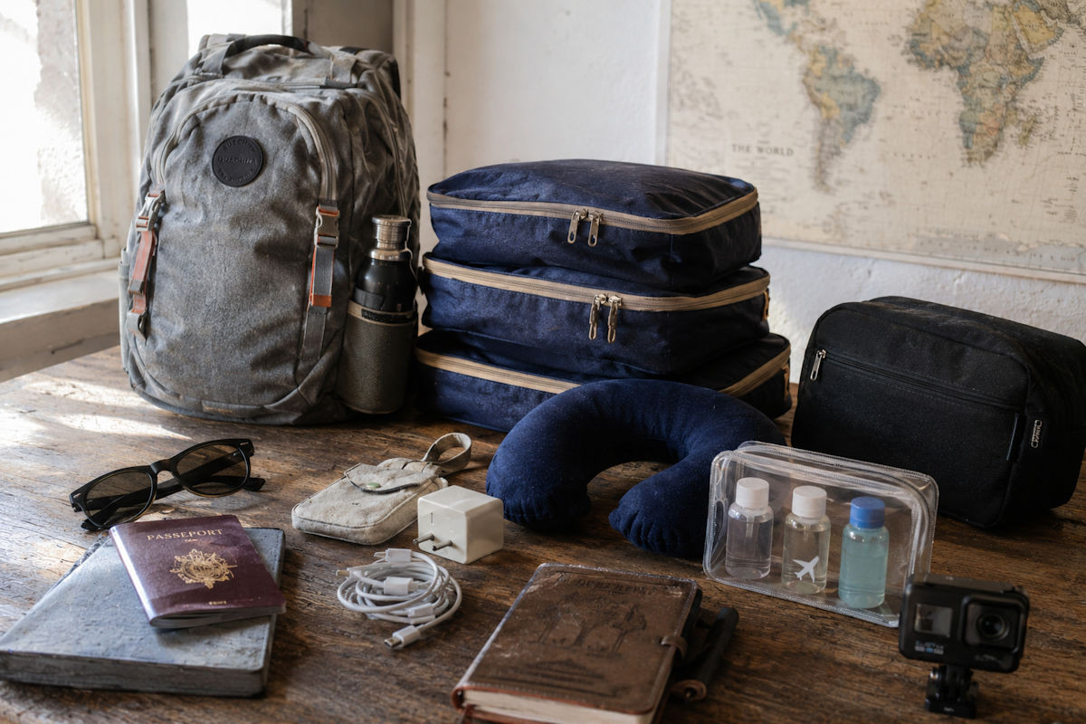 Accessoires de voyage disposés à côté d'une valise cabine : passeport, coussin de nuque, masque de sommeil et trousse de toilette